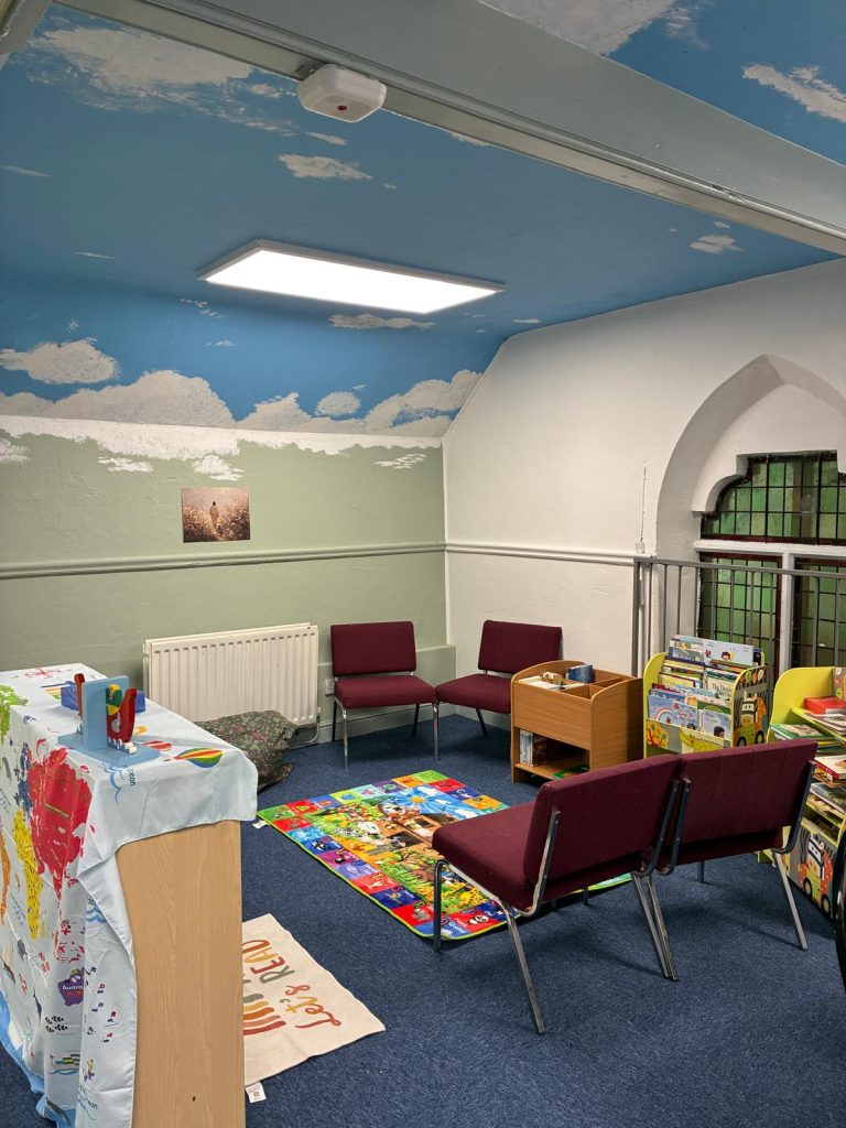 The cosy reading corner in the King’s Kids room, with a painted sky ceiling, a bright alphabet rug, chairs and shelves of children’s books